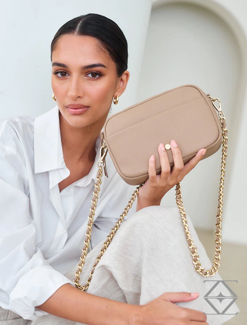 Woman holding a beige handbag with a gold chain strap against a light background