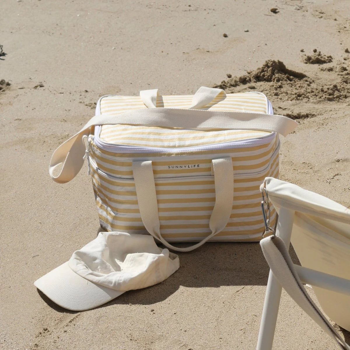 Beige and white striped bag with 'Sunnylife' branding on a sandy beach.