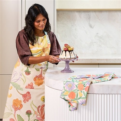 Woman in a kitchen wearing a floral midsummer apron, preparing a dessert.