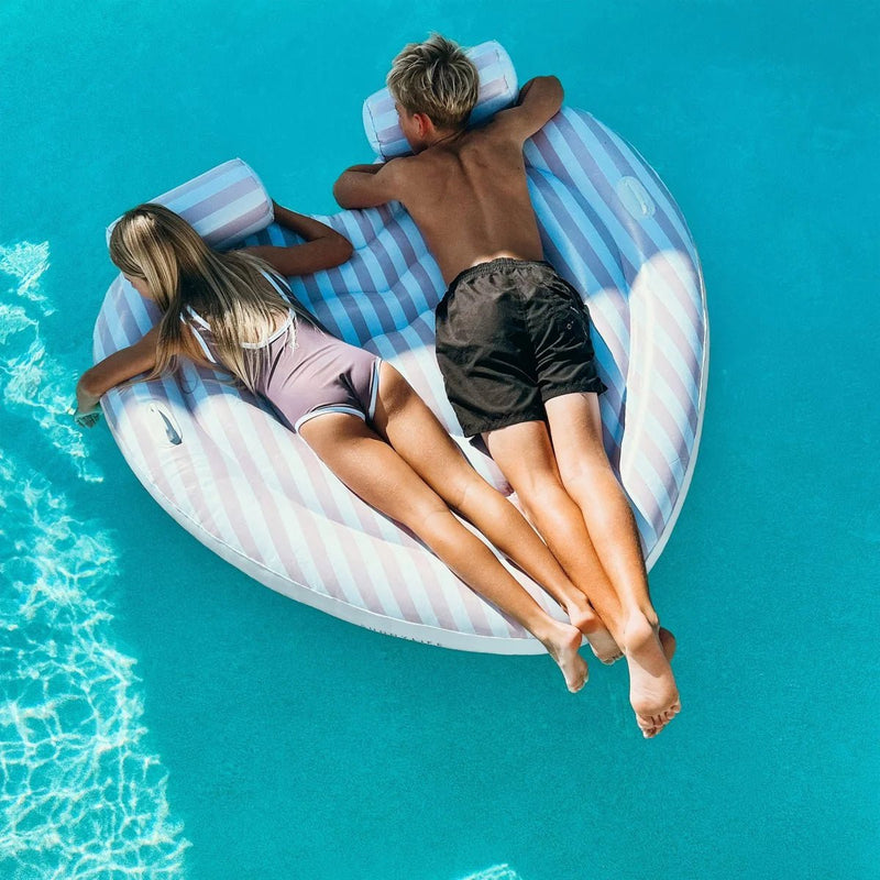 Two people lying on a striped pool float in clear blue water