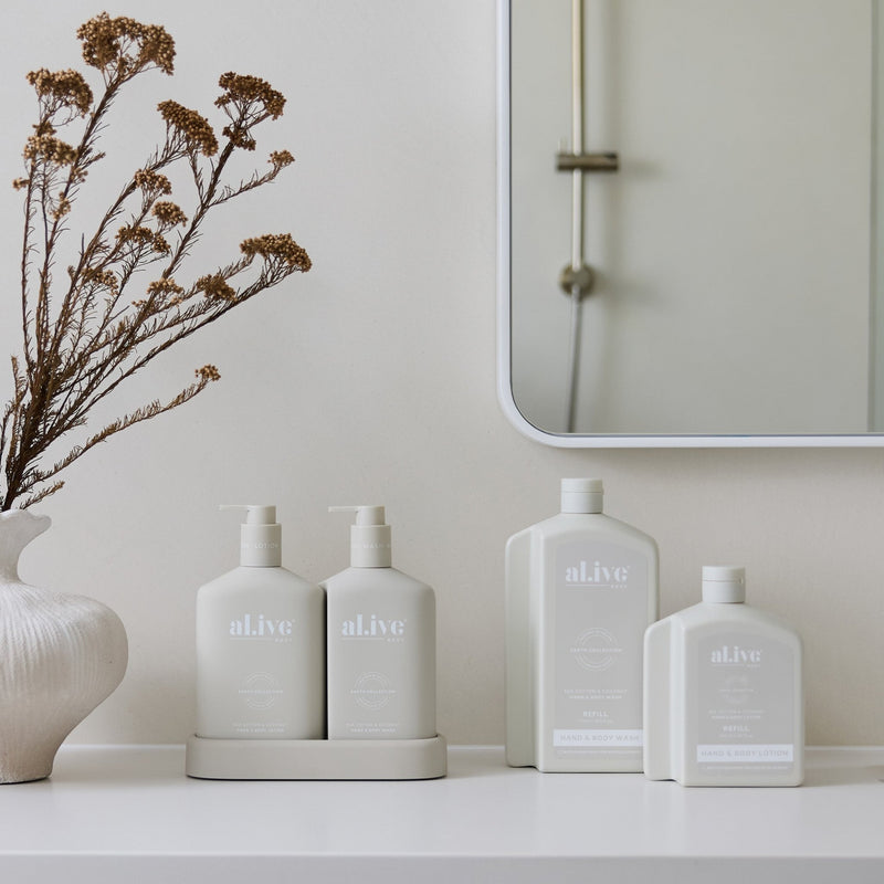 Set of 'alive' skincare bottles on a bathroom counter with a mirror and decorative vase.