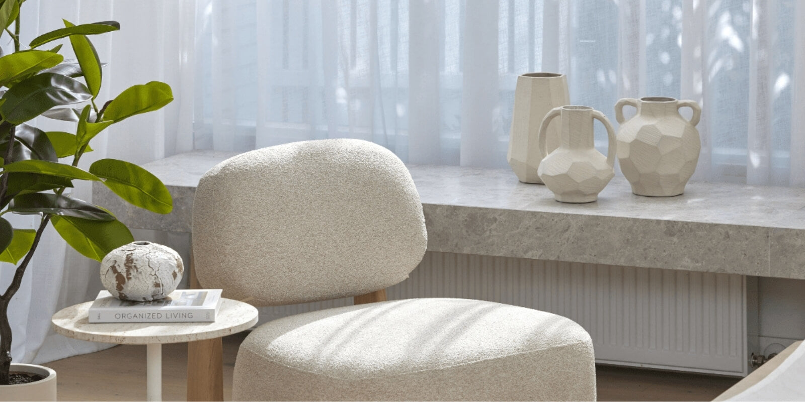 Beige chair and ottoman with decorative vases on a table in a room with curtains.