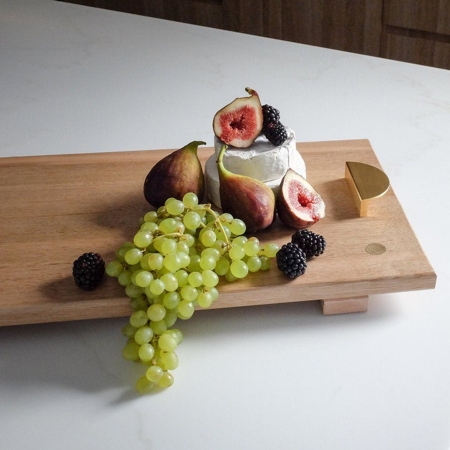 Wooden cutting board with fruits and a block of cheese on a white surface